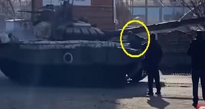 A Ukrainian man kneels in front of marauding Russian tank